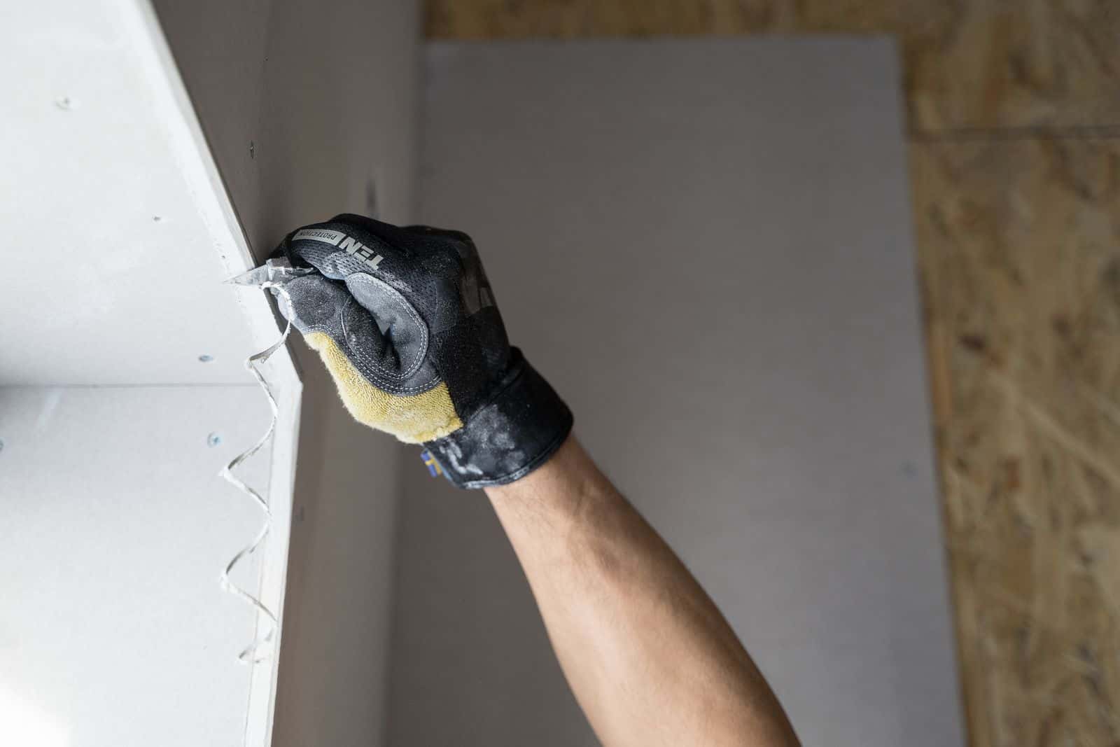 Gloved hand finishing new drywall during water damage repairs